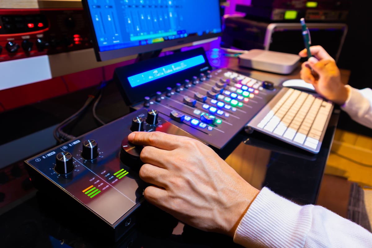 producer, editor hand tweaking volume knob on audio interface for monitoring audio signal from computer while mixing audio track on video footage in post production studio