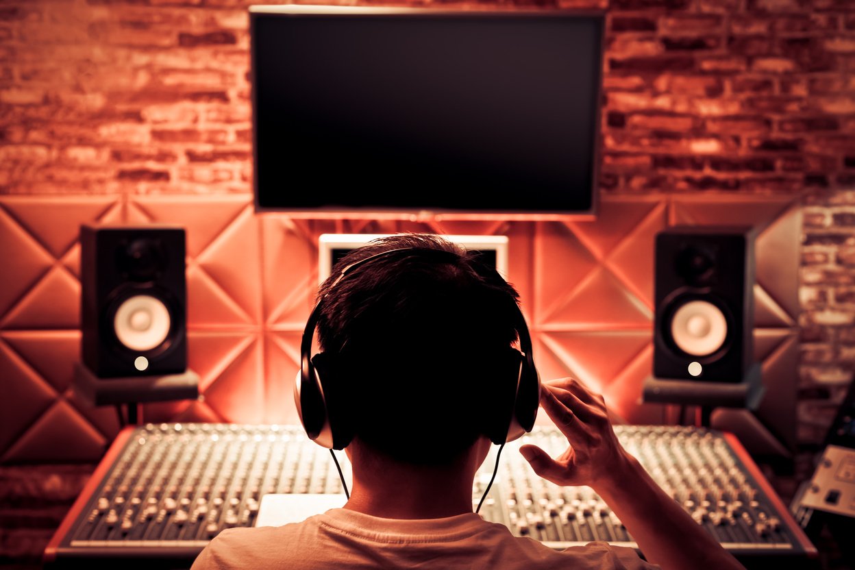 back of asian male music producer working on audio mixing console in recording studio. music production, broadcasting, post production concept